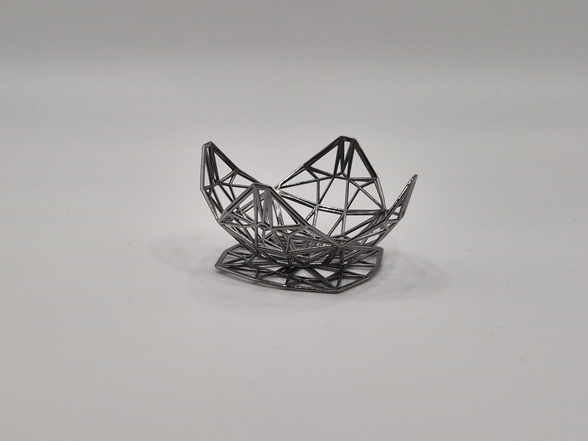 Geometric silver object with an open lattice structure on a white background