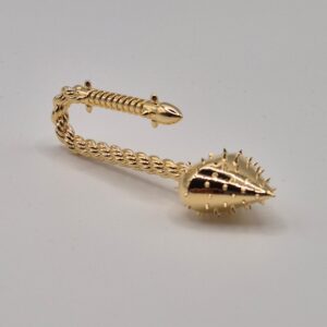 Intricately cast brass object resembling a curved, spiked creature or weapon, showcasing high detail and a polished golden finish.