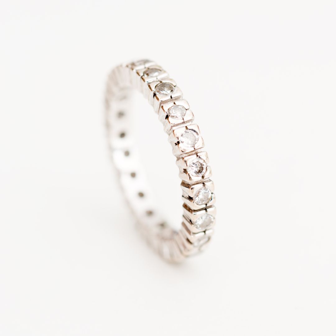 Platinum eternity ring with continuous row of set gemstones on a reflective white surface.